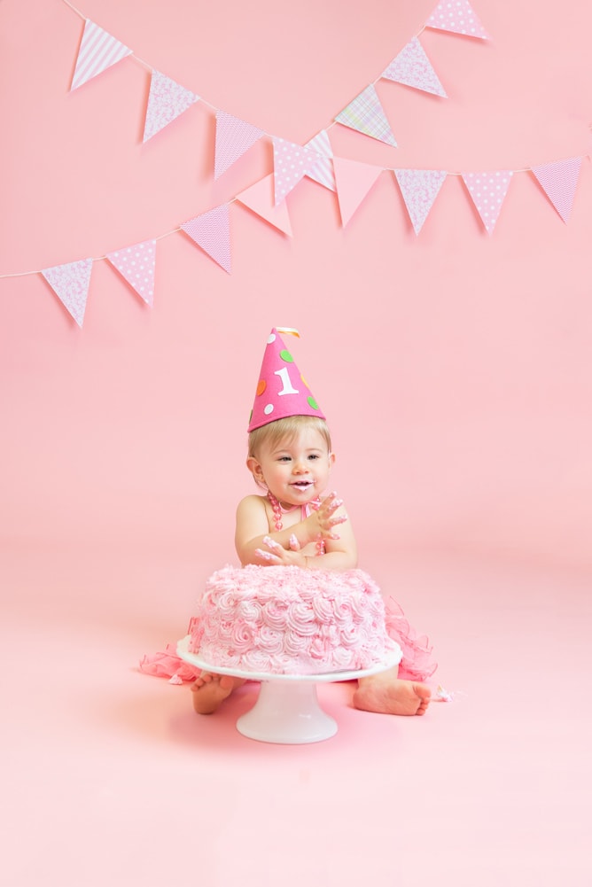 baby girl clapping hands with pink cake