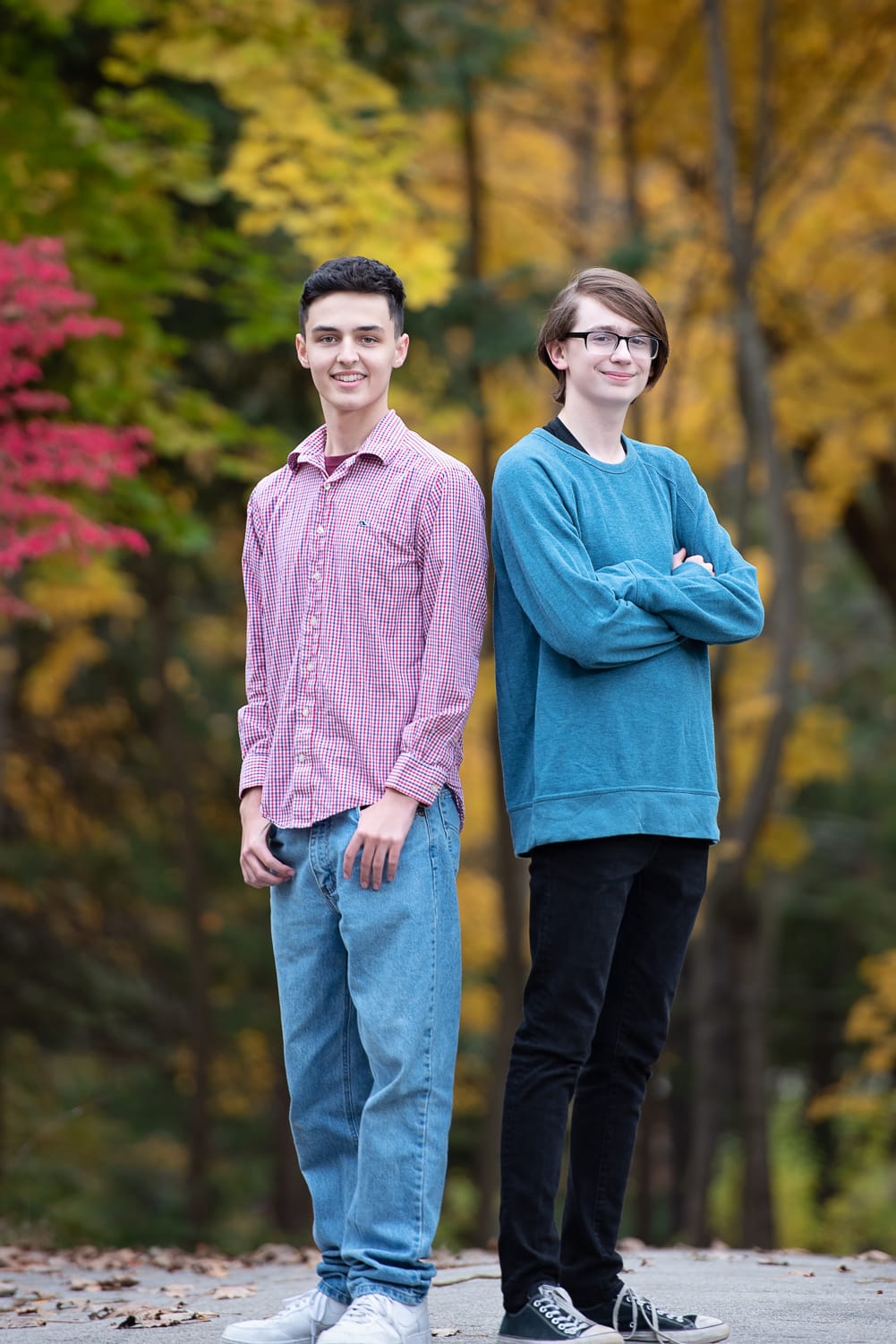 Two high school seniors standing together on the path with red and yellow autumn foliage behind them at Benson Park in Hudson NH