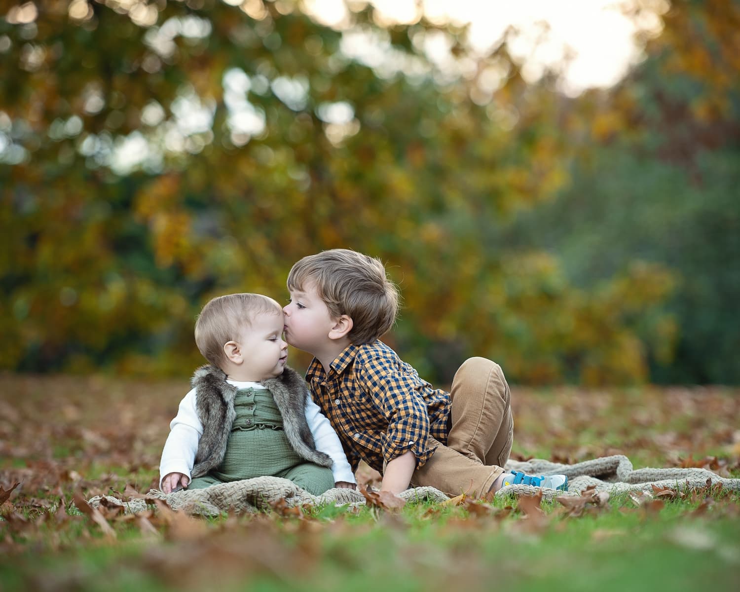 Two young brothers on a blanket in fallen leaves in autumn in Concord MA