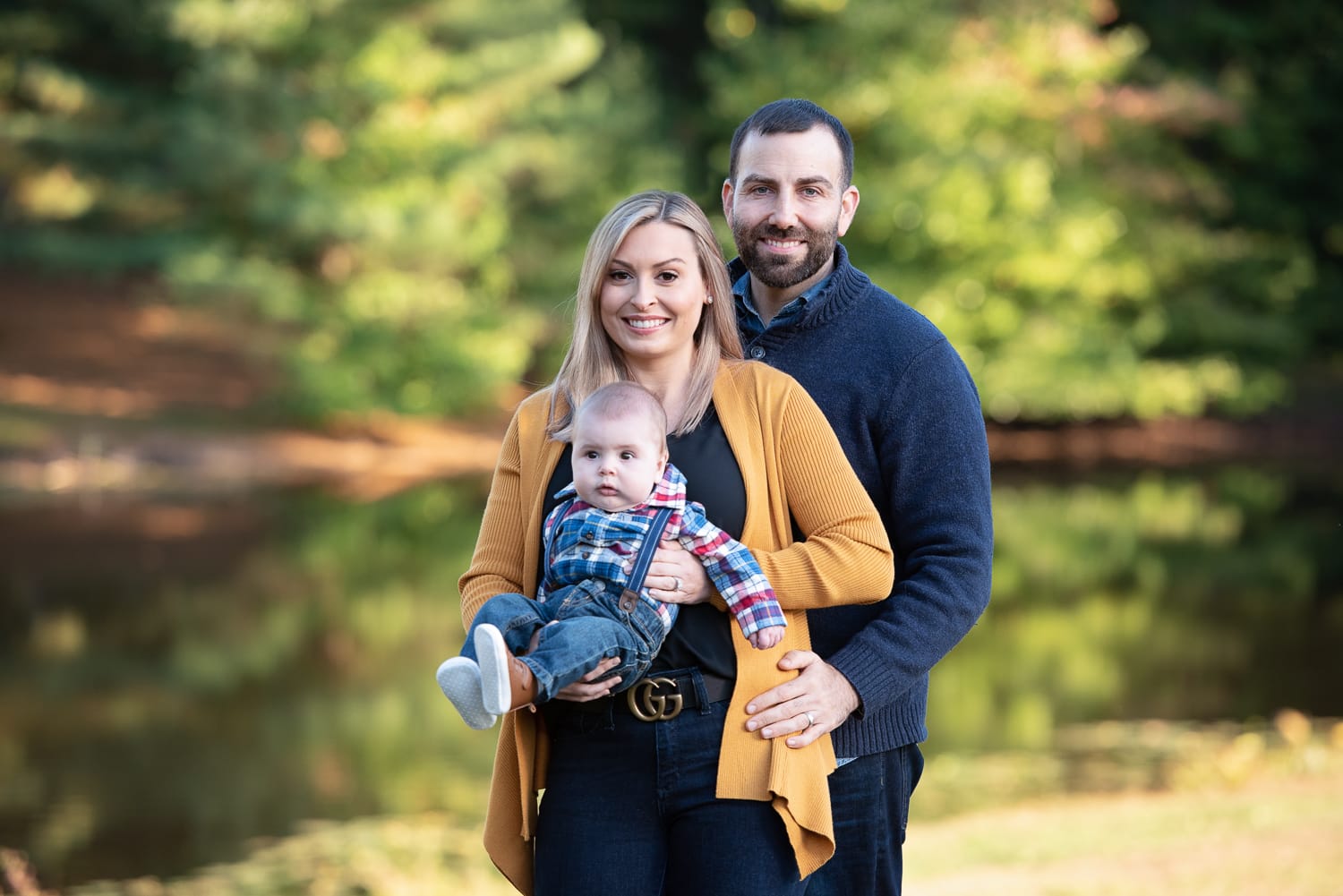Parents holding their baby beside Meadow Pond in autumn at Great Brook Farm State Park in Carlisle MA