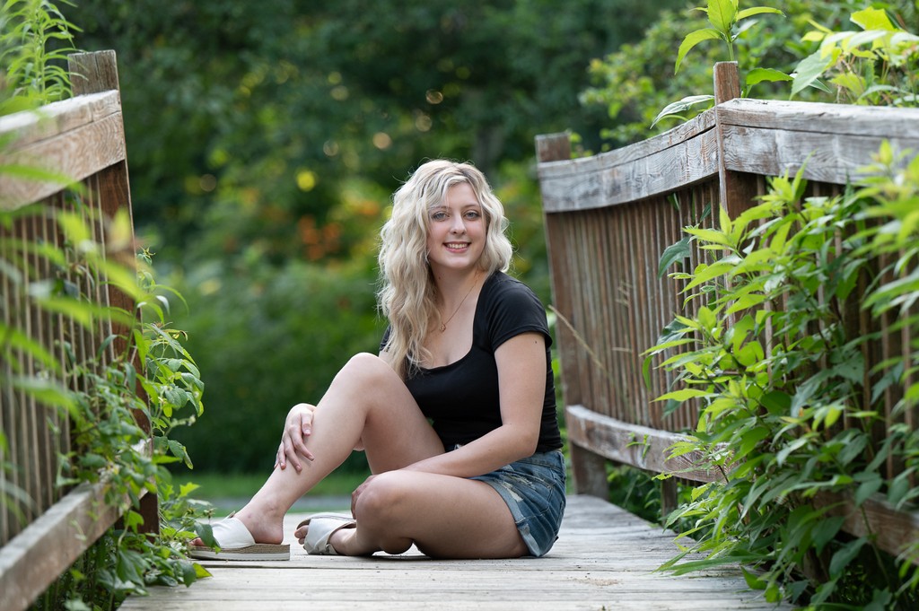 Senior portrait seated on the wooden boardwalk bridge at Acton Arboretum in Acton MA