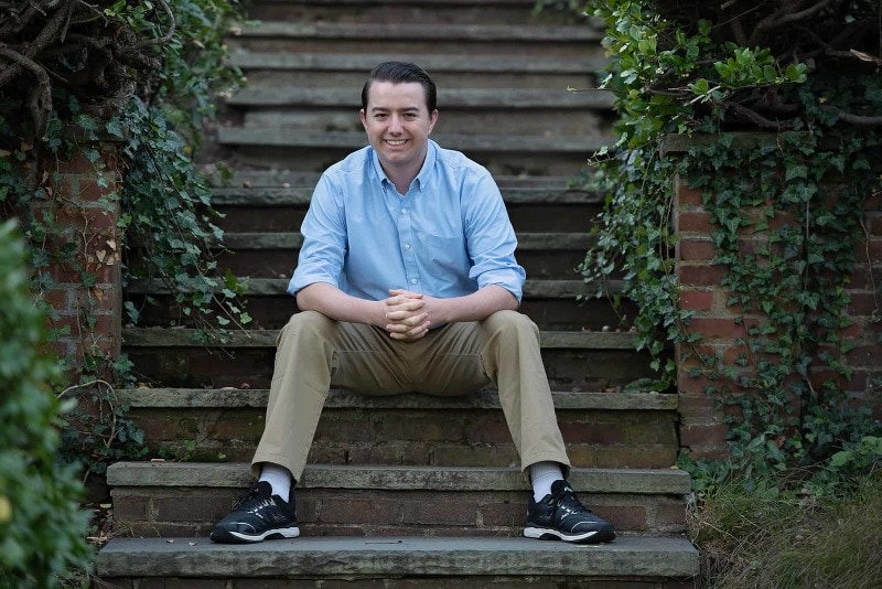 High school senior boy seated on stone steps between ivy covered brick pillars in Concord Massachusetts