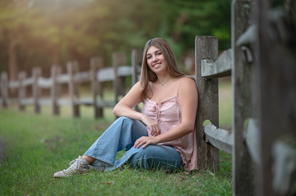High school senior girl seated against a split-rail fence in the field at Great Brook Farm in Carlisle MA