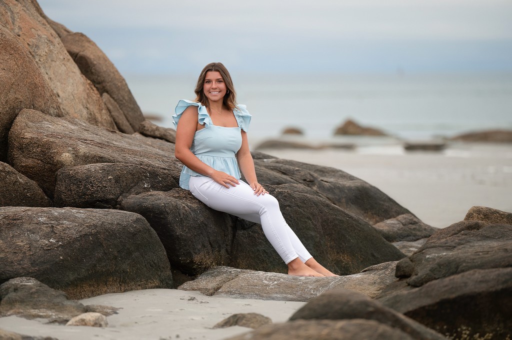 High school senior girl seated among the granite boulders at Wingaersheek Beach in Gloucester MA