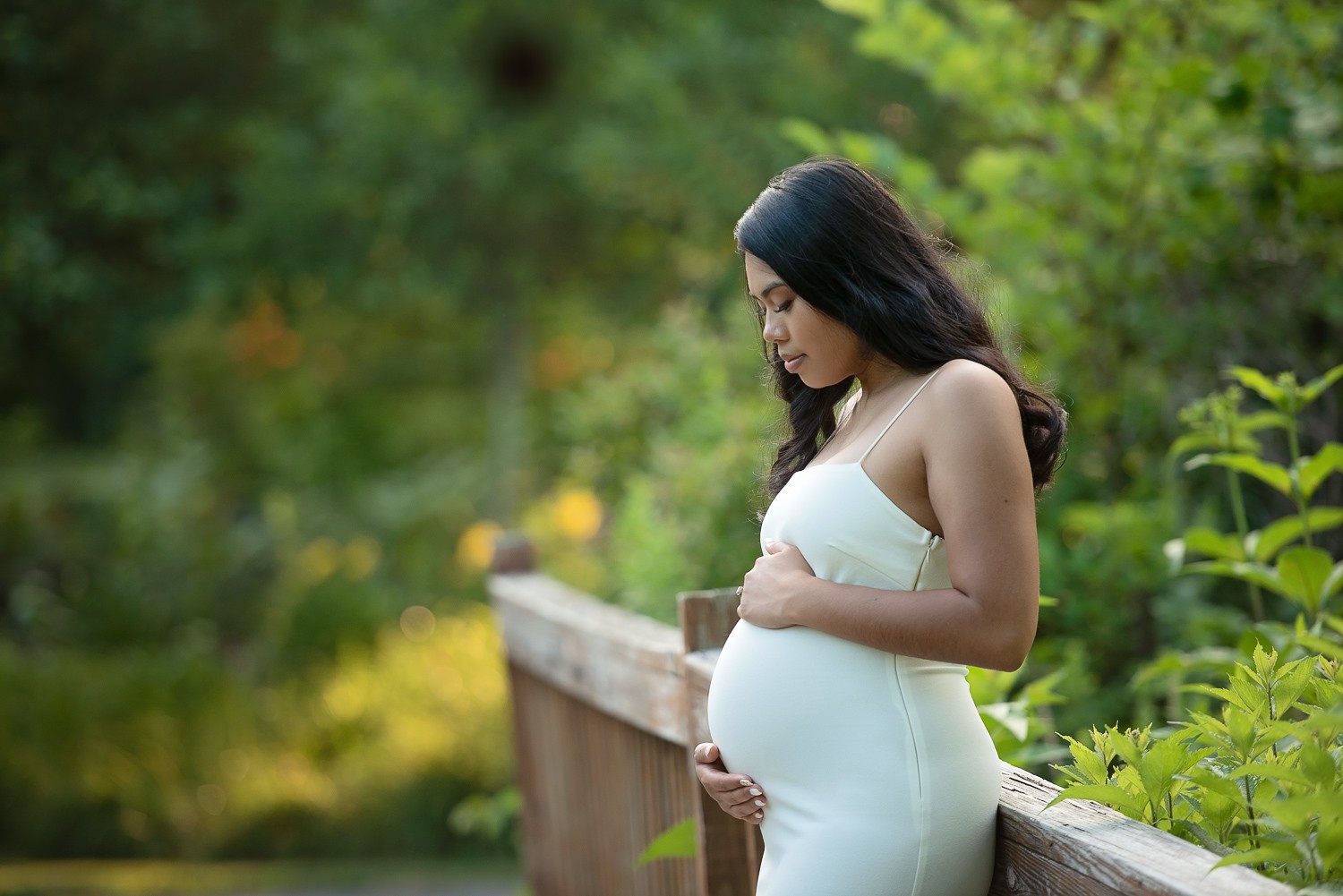 Expecting mother on the wooden boardwalk rail at Acton Arboretum in Acton MA