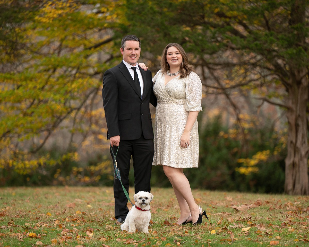 Couple in formal dress with their small white dog under autumn trees in Concord Massachusetts