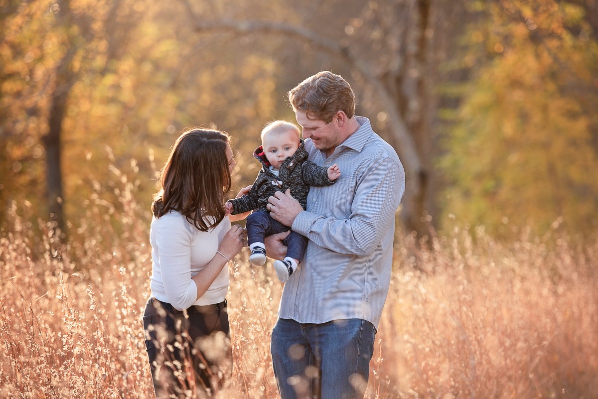 Parents holding their baby in backlit autumn grass in Concord Massachusetts