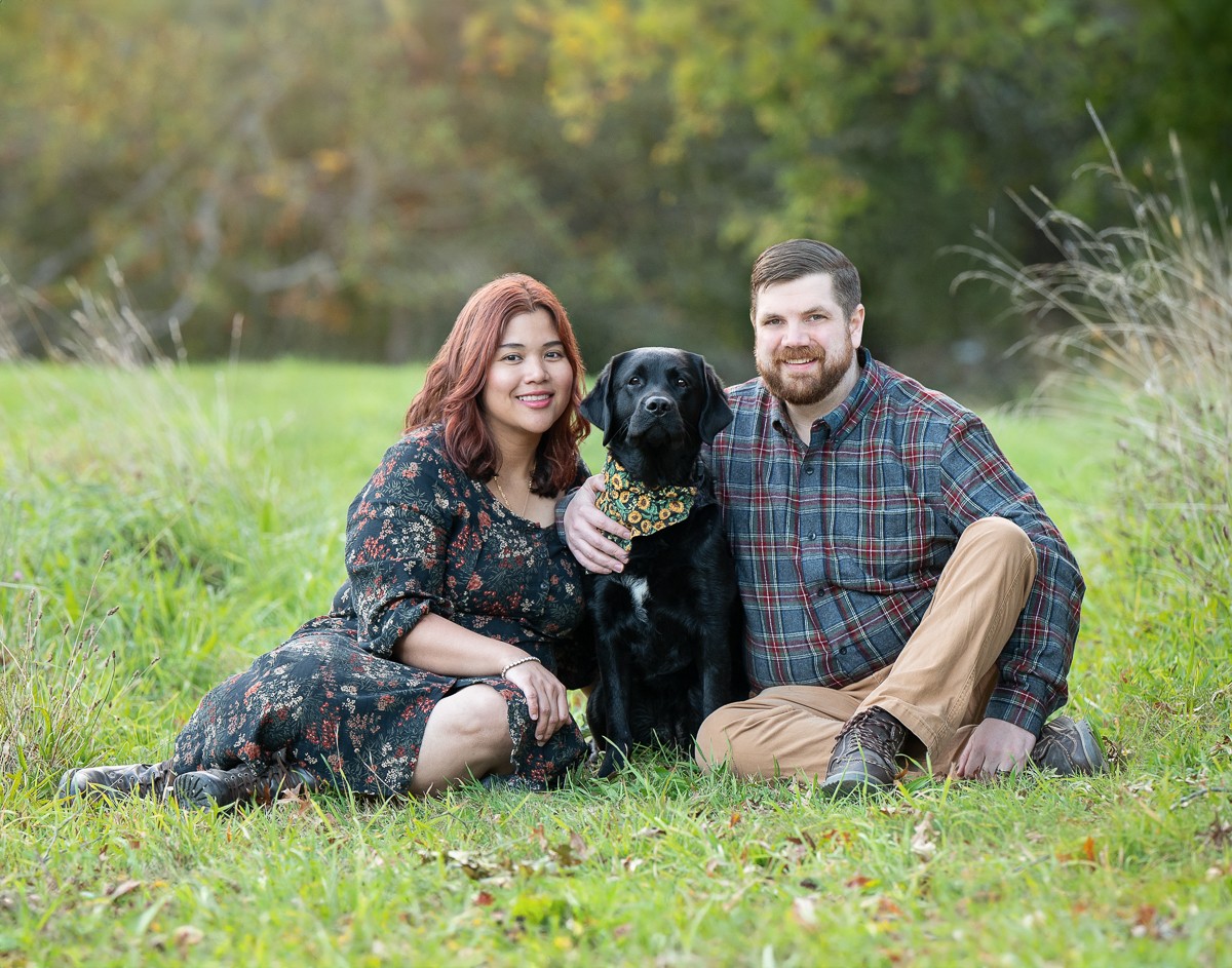 Couple seated in the meadow with their black Labrador at the Old North Bridge in Concord Massachusetts