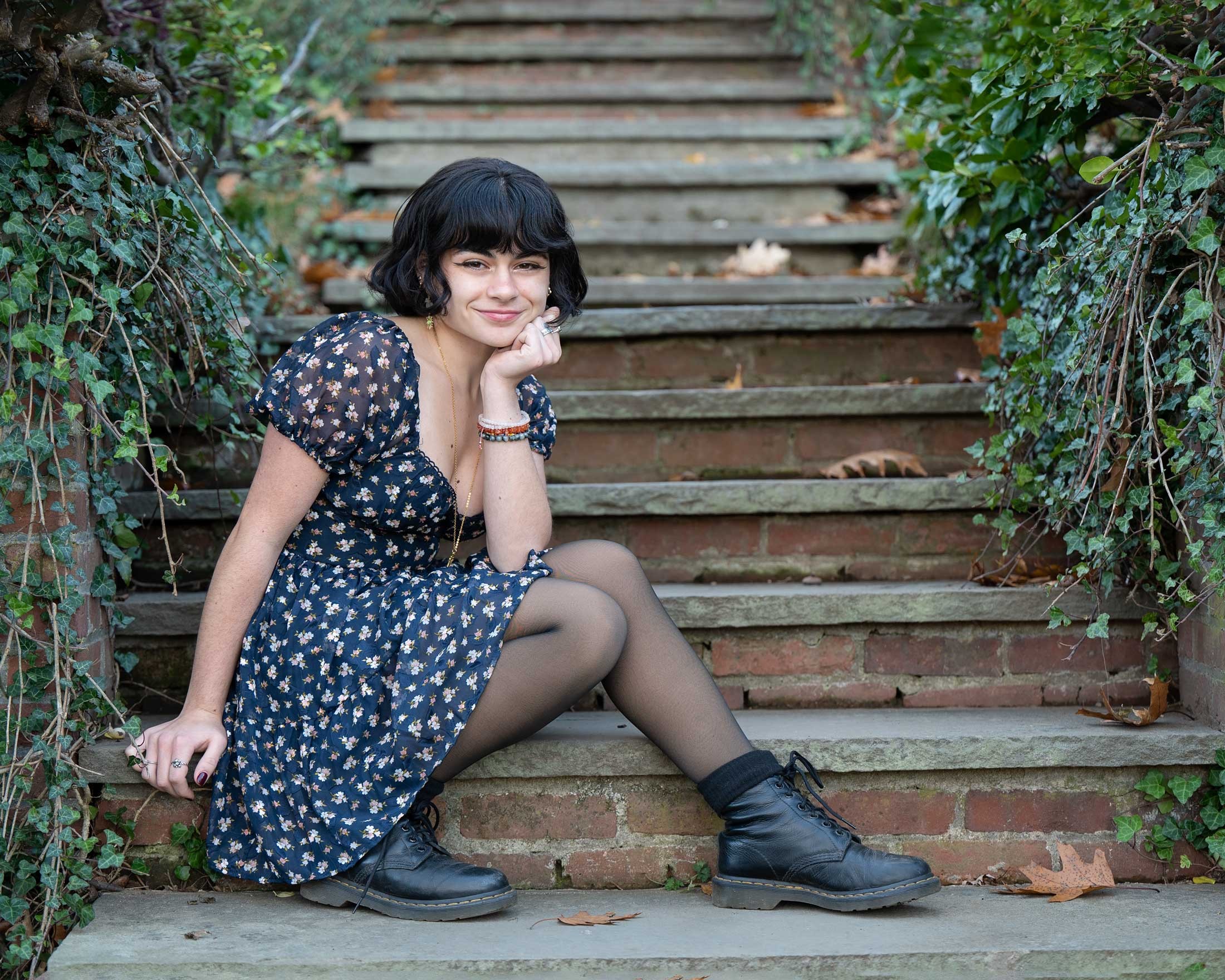 High school senior girl in a floral dress seated on ivy covered stone steps in autumn in Concord MA