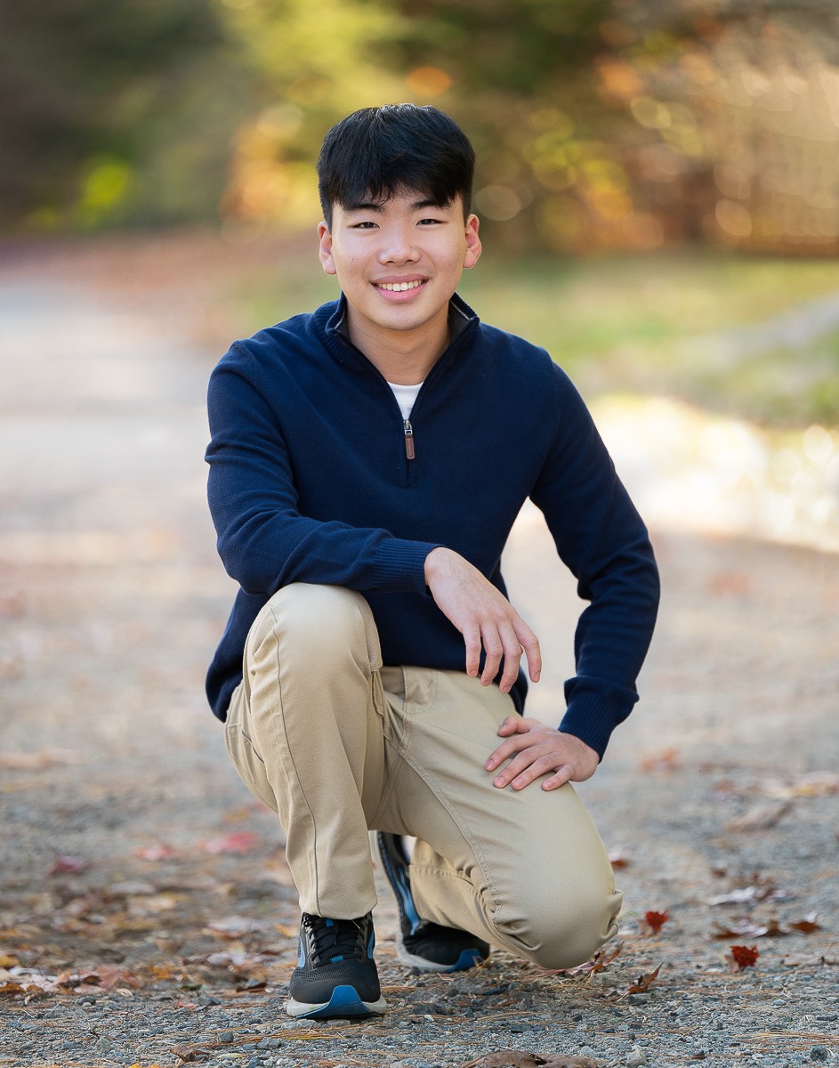 High school senior boy kneeling on the gravel farm road at Great Brook Farm State Park, Carlisle Massachusetts