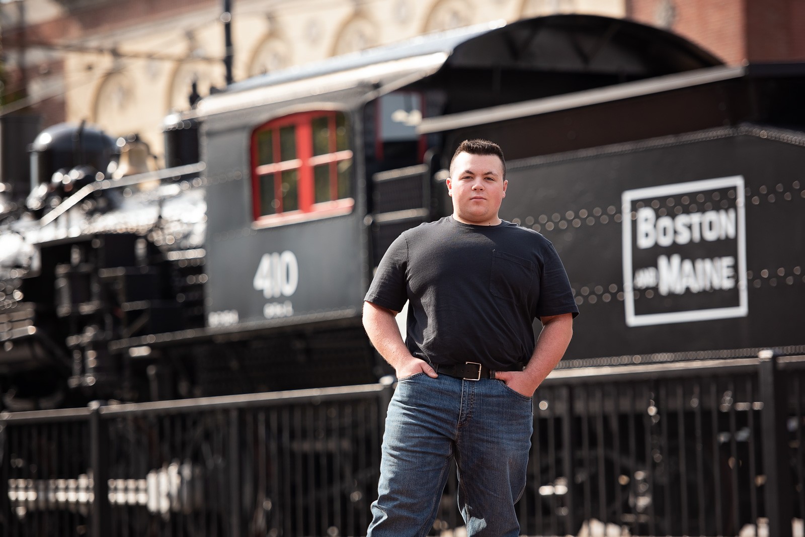 High school senior beside a black Boston and Maine locomotive at Lowell National Historical Park in Lowell MA