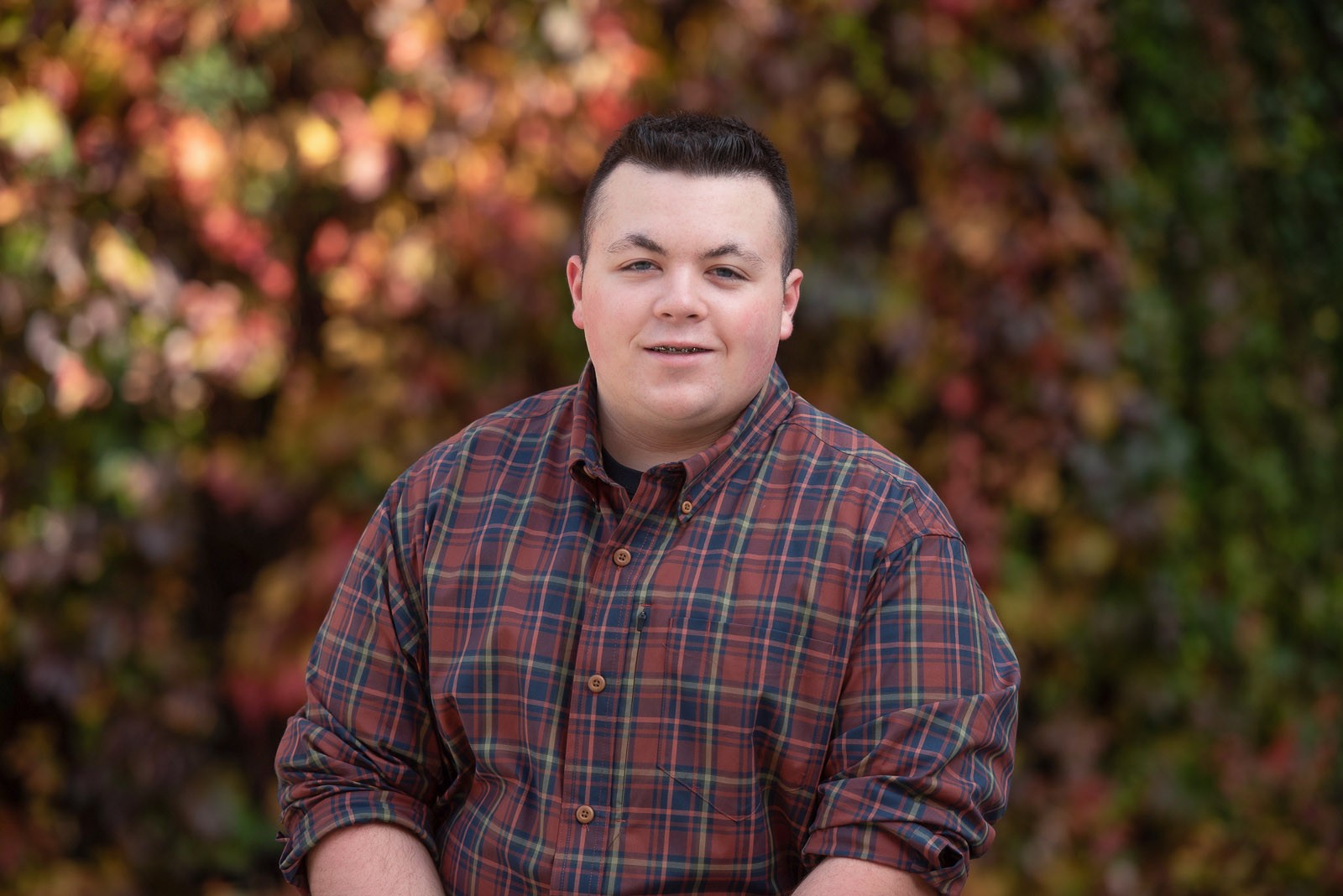 Close autumn senior portrait of a high school boy in a plaid shirt against red and green Boston ivy in Lowell Massachusetts