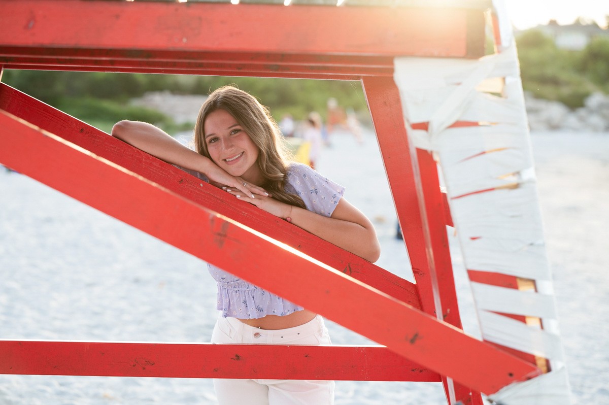 High school senior girl leaning on the red lifeguard chair at Wingaersheek Beach, Gloucester Massachusetts