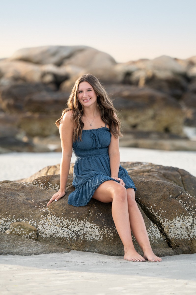 High school senior girl seated on the rocks at the tide line at Wingaersheek Beach in Gloucester MA