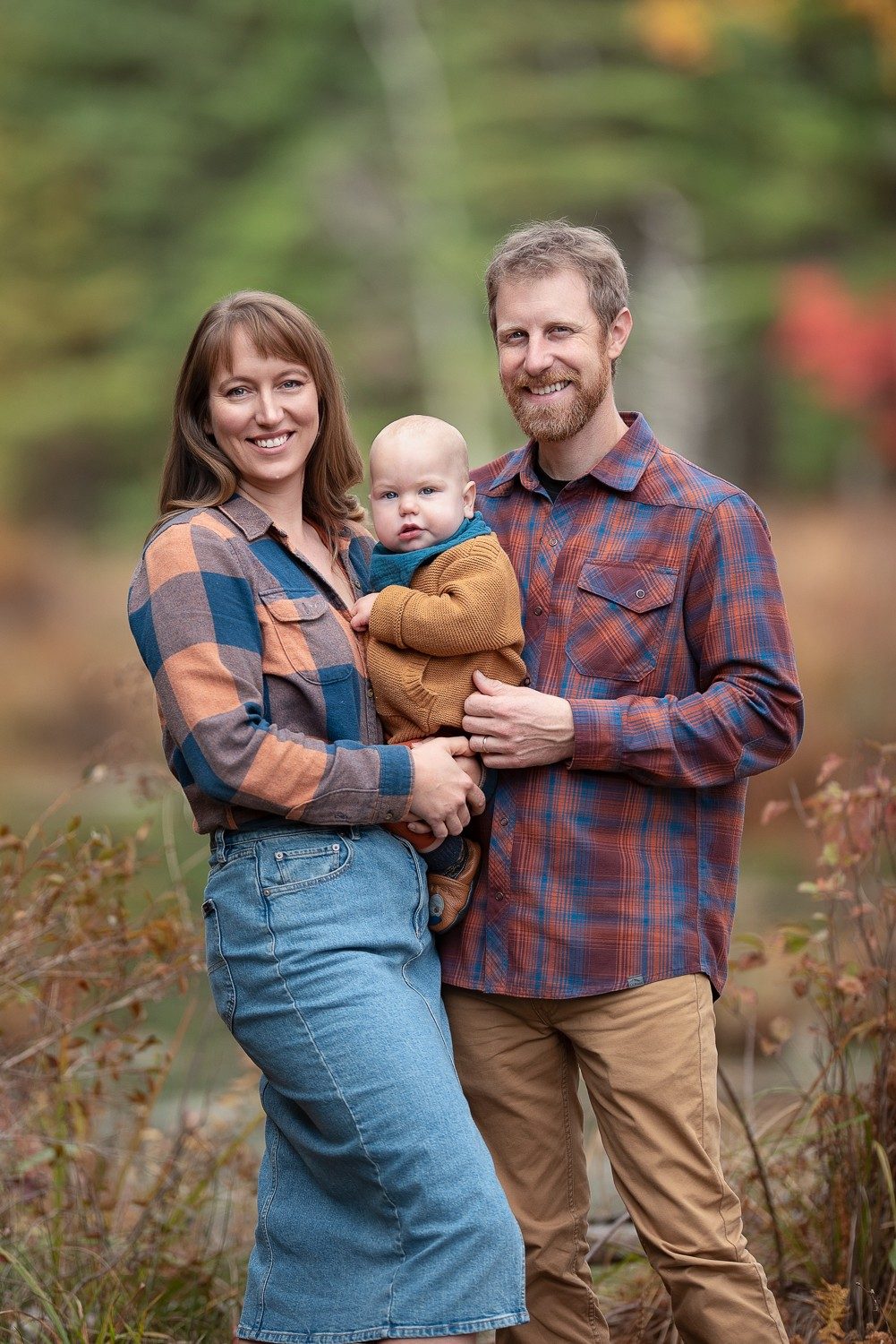 Parents standing with their baby beside still water with red foliage behind at Assabet River National Wildlife Refuge, Sudbury Massachusetts