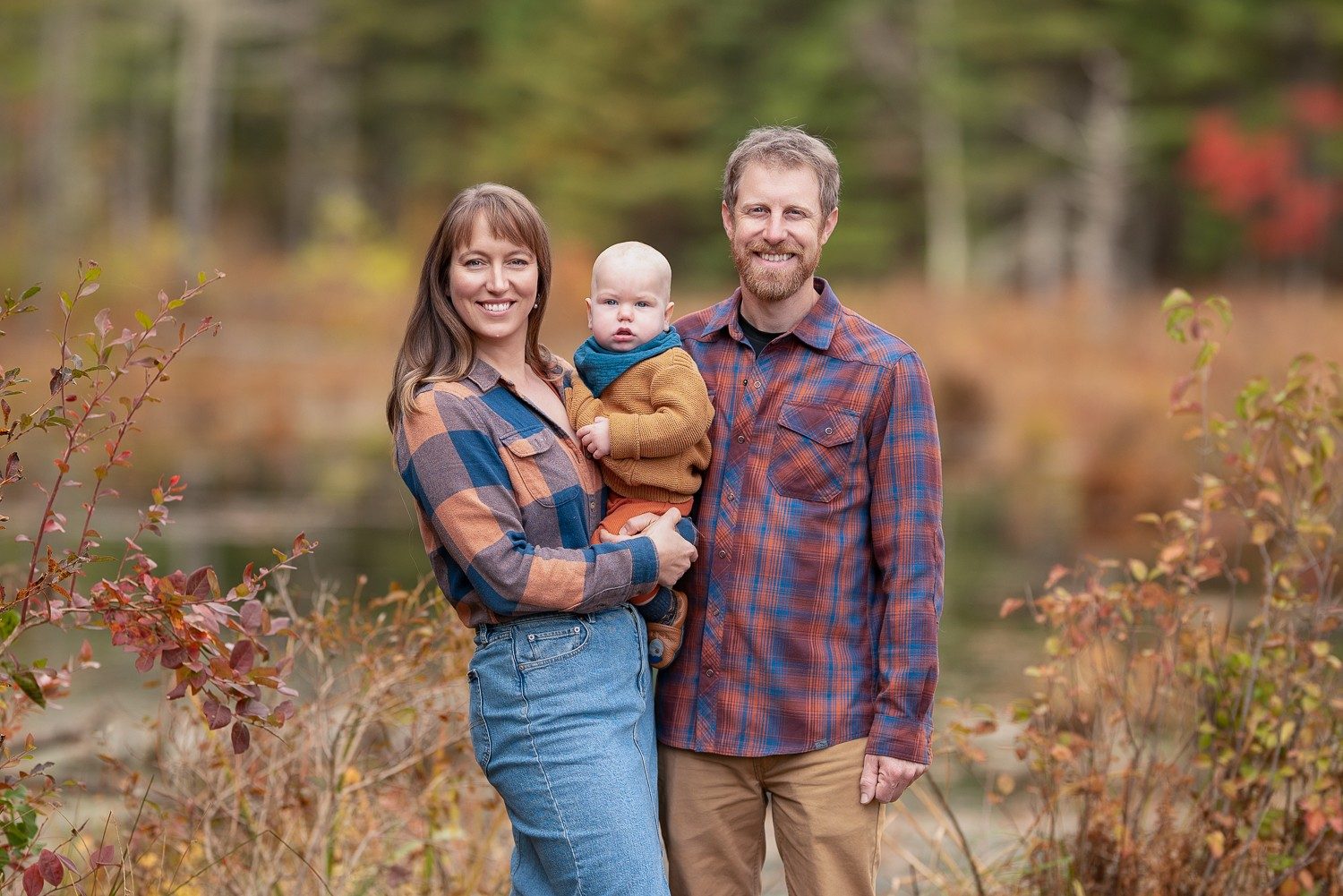 Mother holding her baby beside his father with autumn color behind them at Assabet River National Wildlife Refuge in Sudbury MA