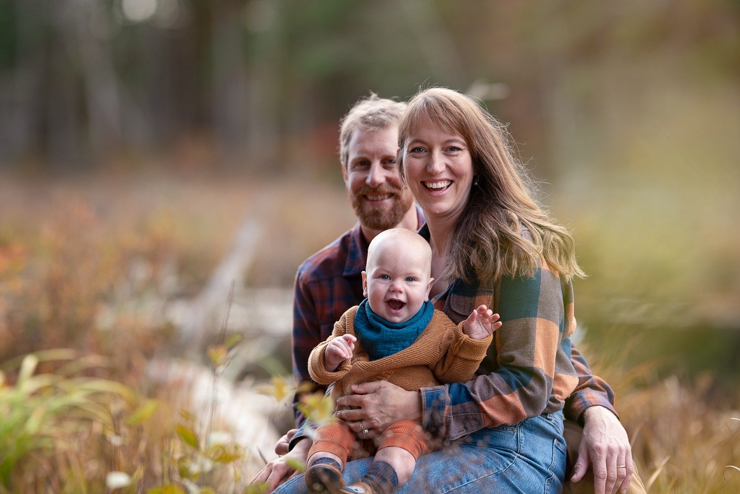 Close portrait of two parents laughing with their baby held between them at Assabet River National Wildlife Refuge, Sudbury Massachusetts