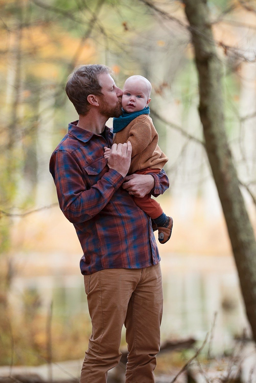 Father lifting his baby to kiss him beside the water in autumn at Assabet River National Wildlife Refuge in Sudbury MA