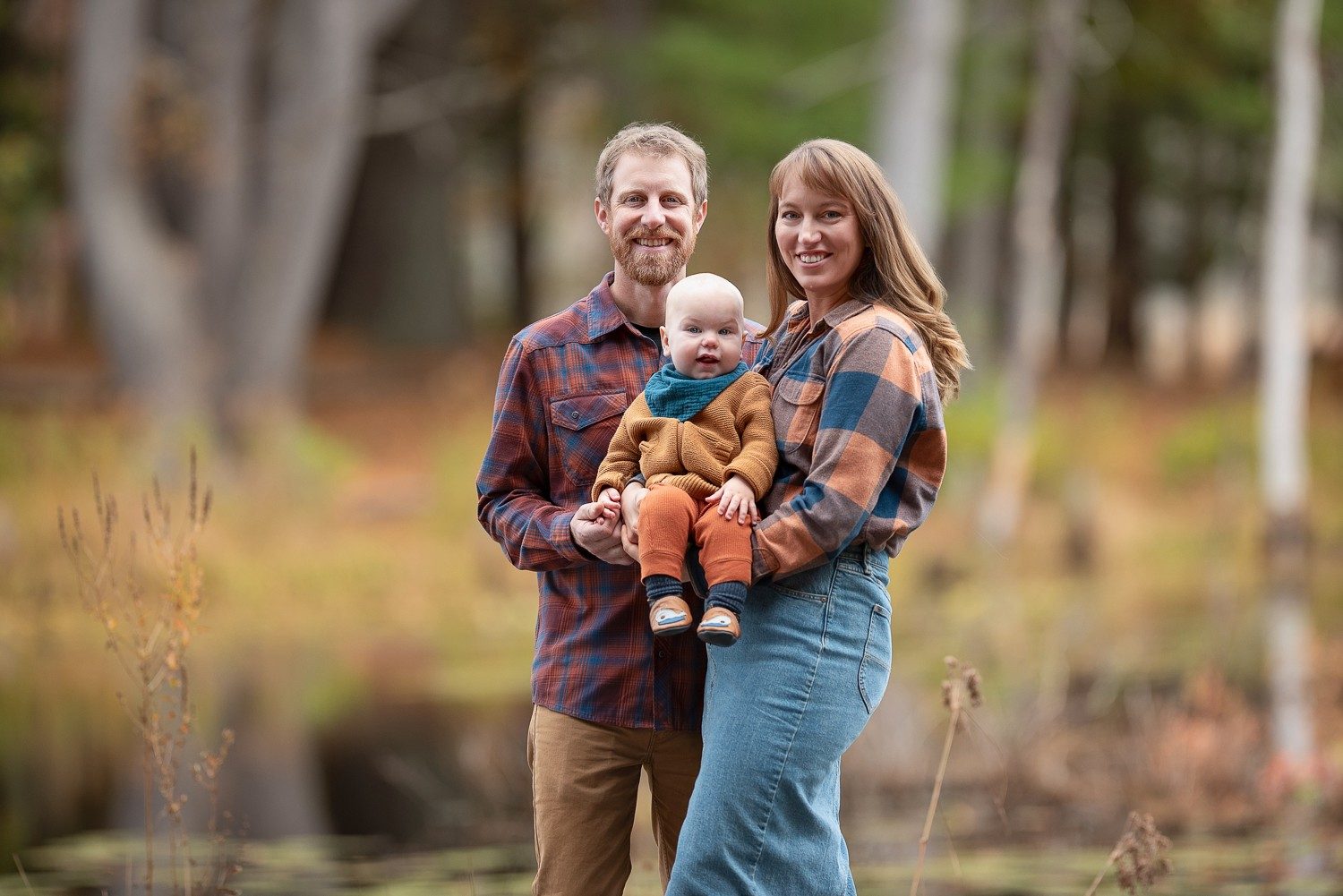Family of three at the water's edge under tall trees in autumn at Assabet River National Wildlife Refuge in Sudbury MA