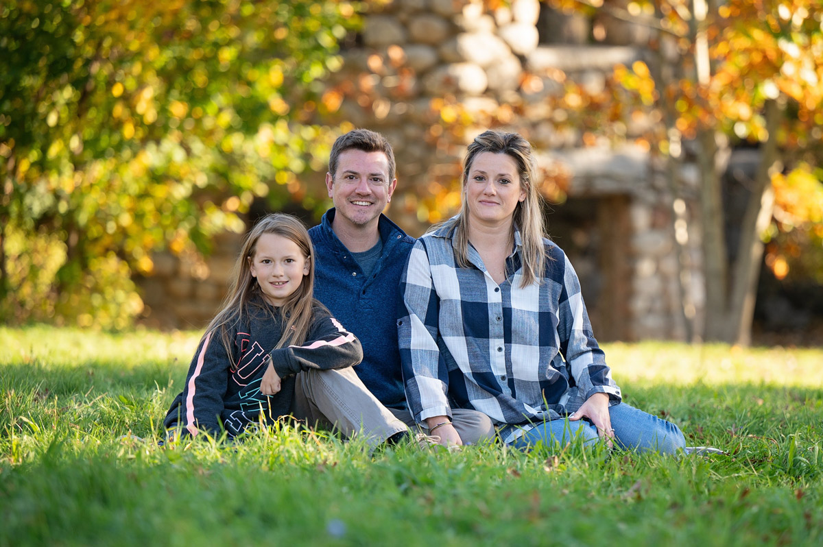 Family sitting on the grass with the stone ruins of Bancroft's Castle behind them in Groton MA