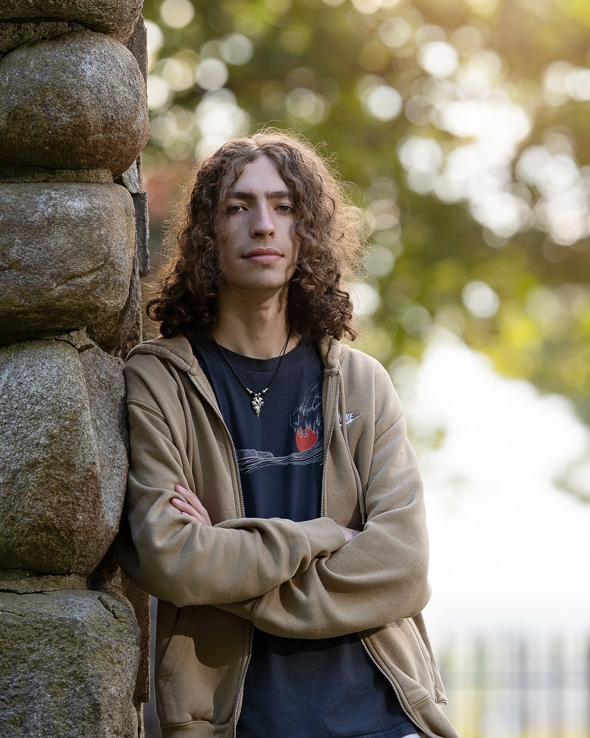 High school senior with long curly hair leaning against a stone pillar at Bancroft's Castle in Groton MA