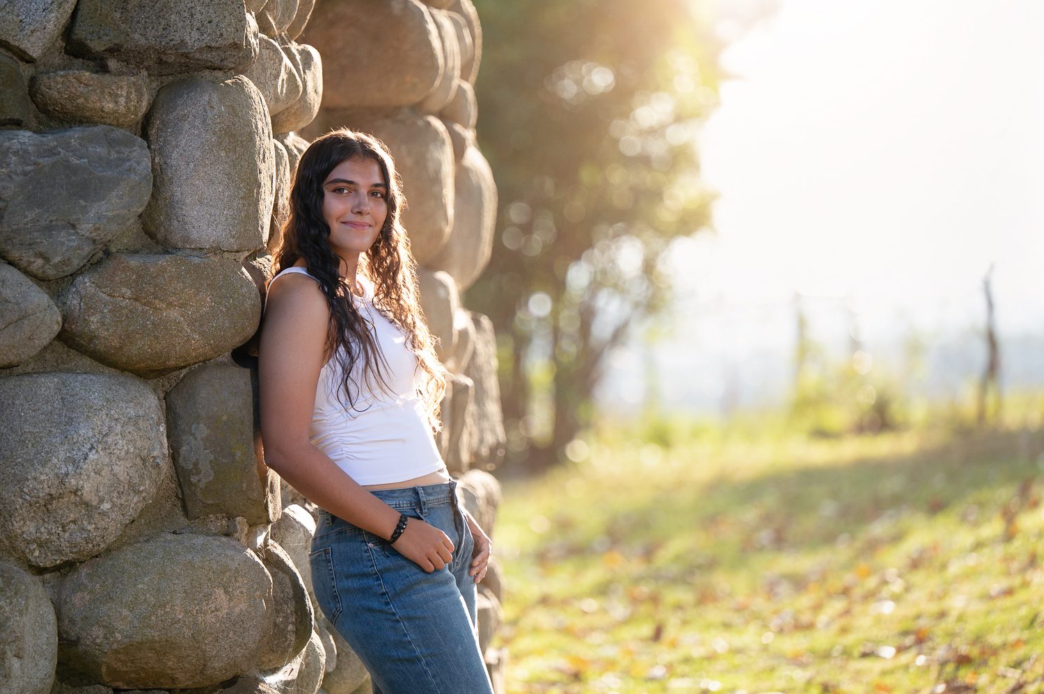 High school senior leaning against the rounded stone tower of Bancroft's Castle with the field behind in Groton MA