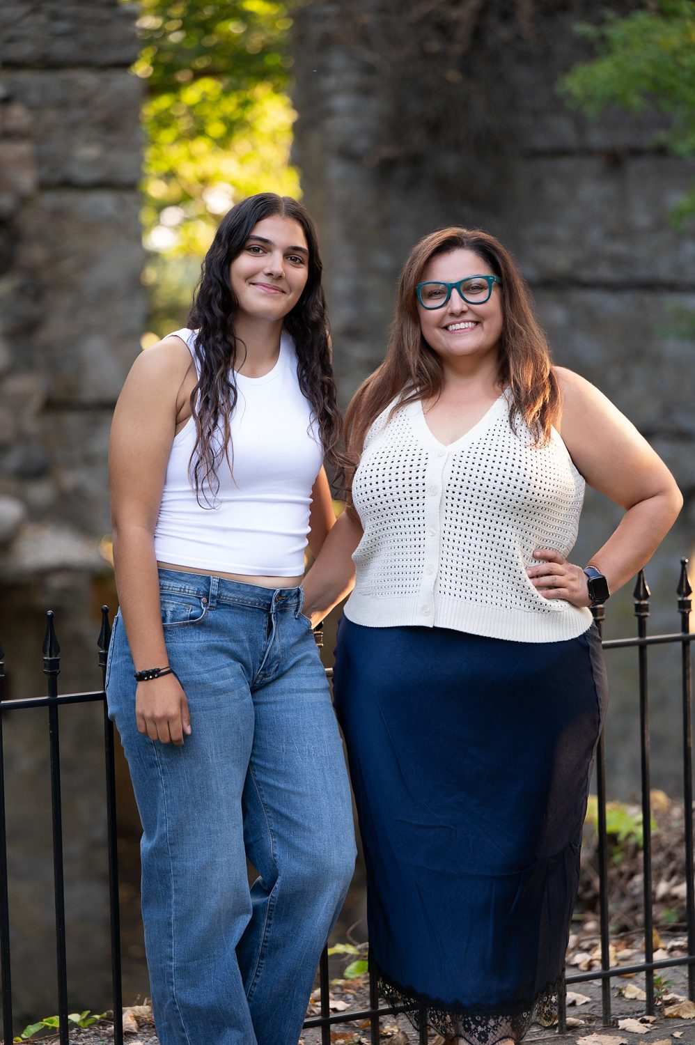 Two young women standing together against the stone wall and iron fence at Bancroft's Castle, Groton Massachusetts