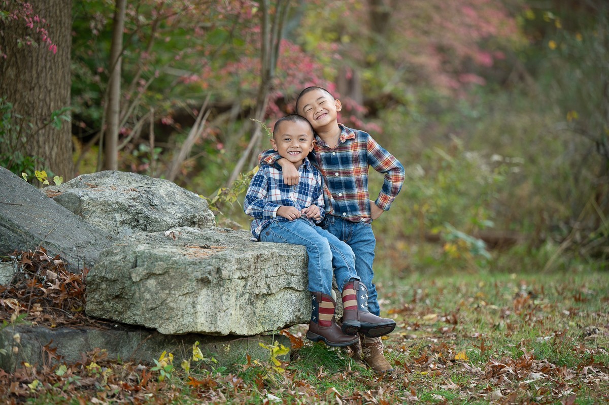 Mother with her two young sons in blue plaid seated on a glacial boulder at Bartlett Park in Chelmsford Massachusetts in autumn