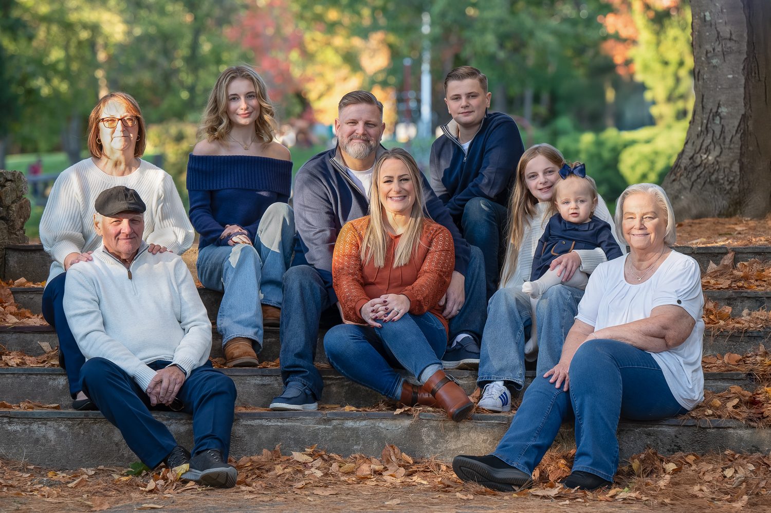 Extended family of twelve seated together on the granite steps in autumn at Benson Park in Hudson NH