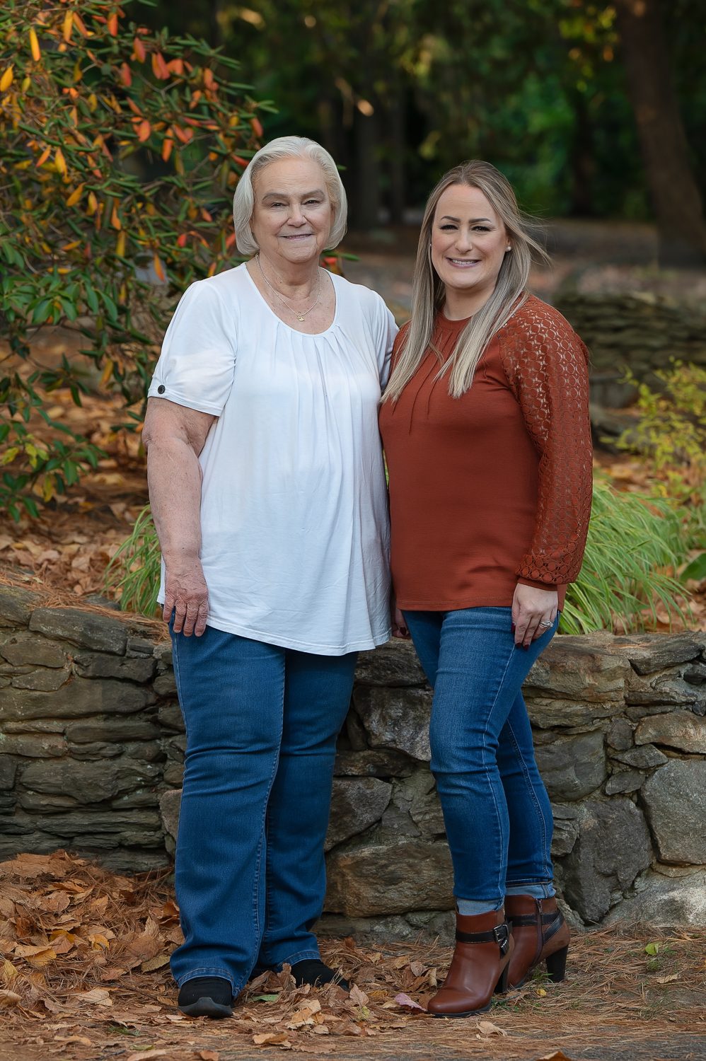 Two women of different generations standing together against a stone wall in autumn at Benson Park, Hudson NH
