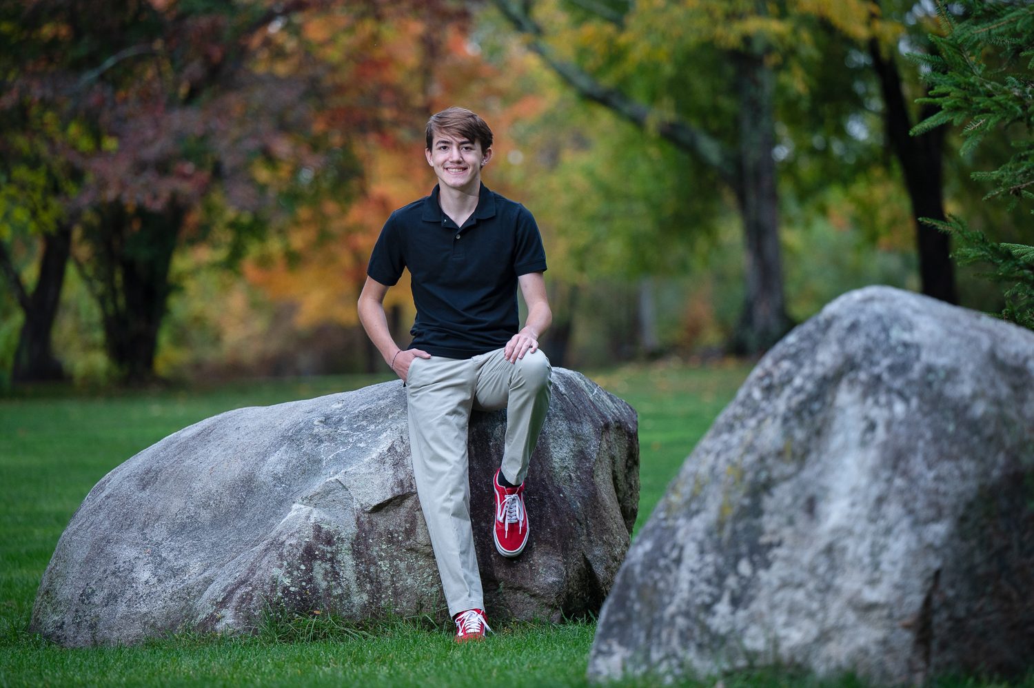 High school senior seated on the glacial boulders in the lawn at Benson Park, Hudson New Hampshire