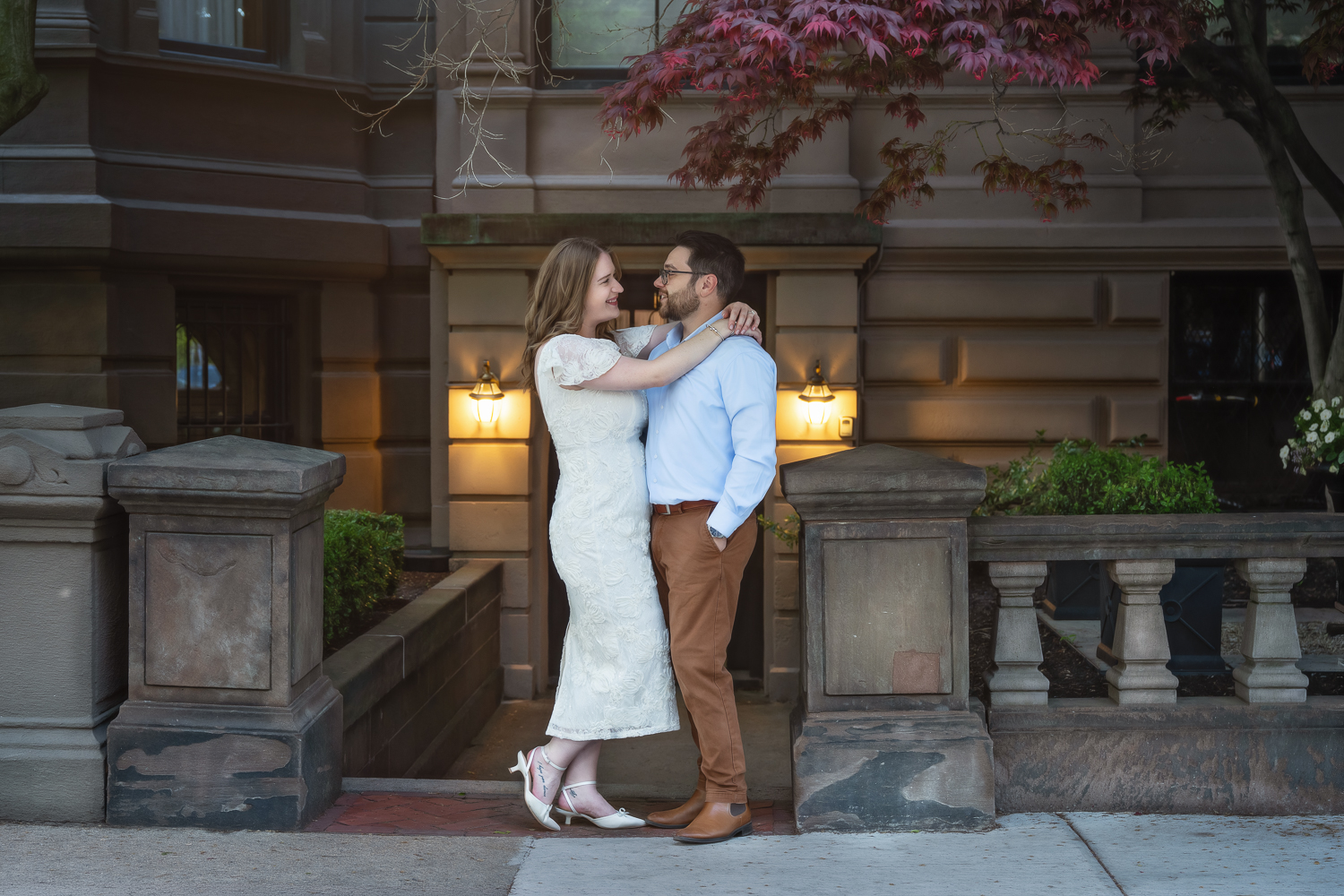Couple standing on the sidewalk in front of a Back Bay brownstone under a flowering tree in Boston Massachusetts