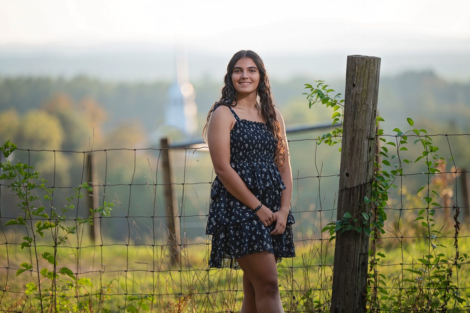High school senior standing beside a weathered pasture fence post on Gibbet Hill with the valley behind in Groton MA