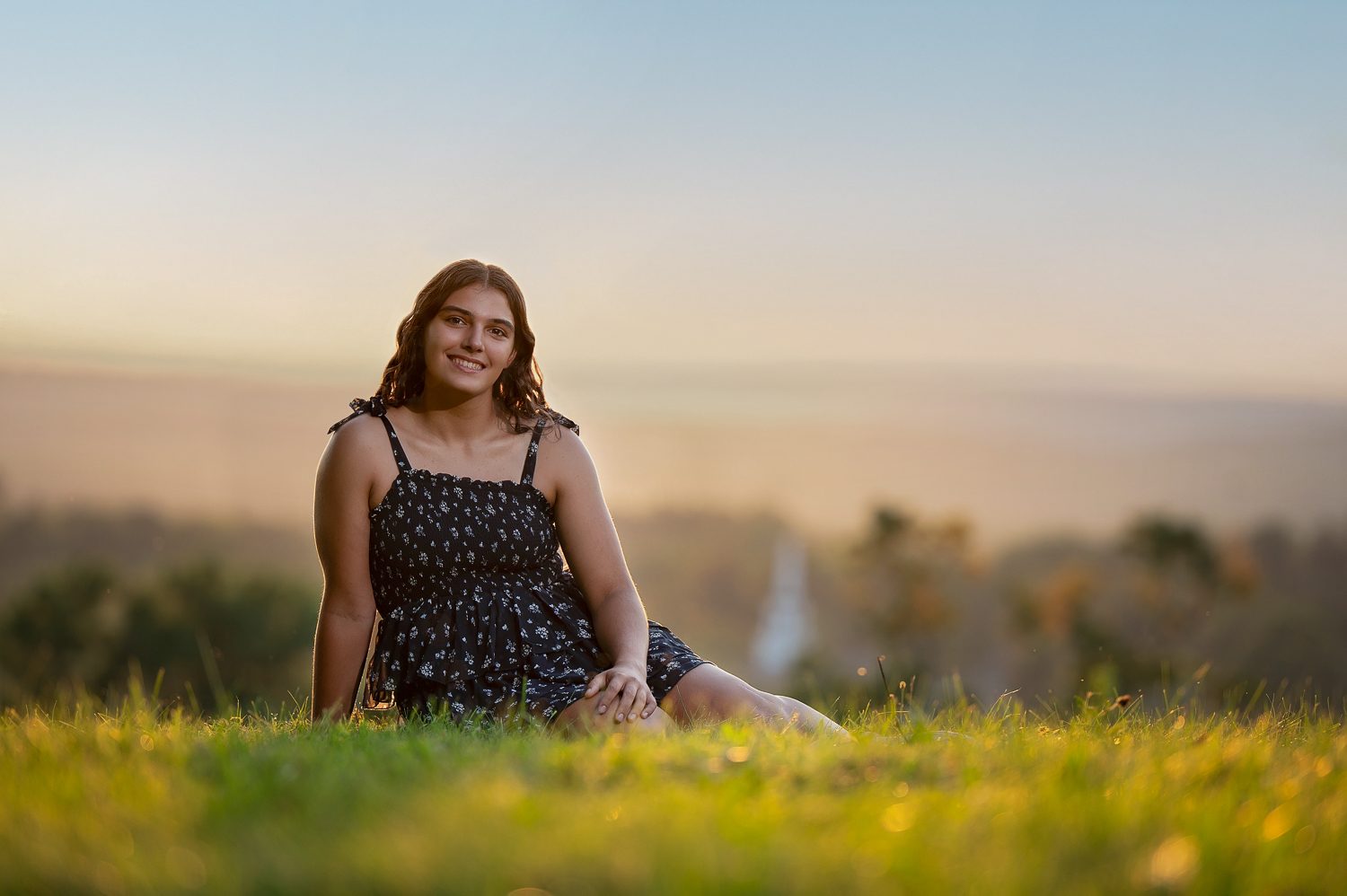 High school senior seated on the summit grass at Gibbet Hill in the last light with the Groton valley behind her