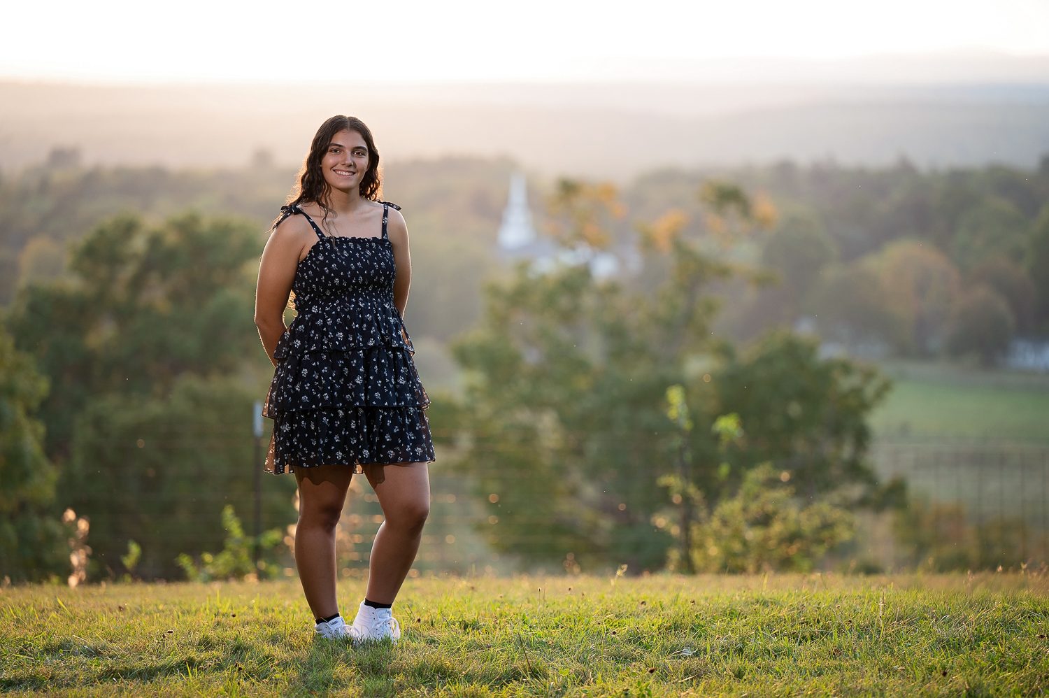 High school senior standing on the summit of Gibbet Hill with the Nashoba Valley and a white church steeple behind her in Groton MA