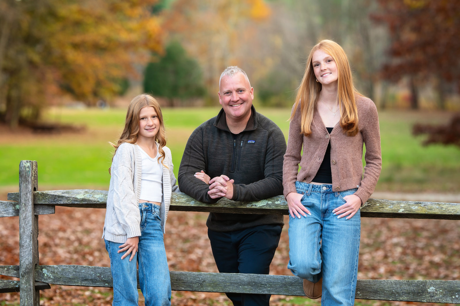 Father and two daughters at a split-rail fence in autumn at Great Brook Farm State Park in Carlisle MA