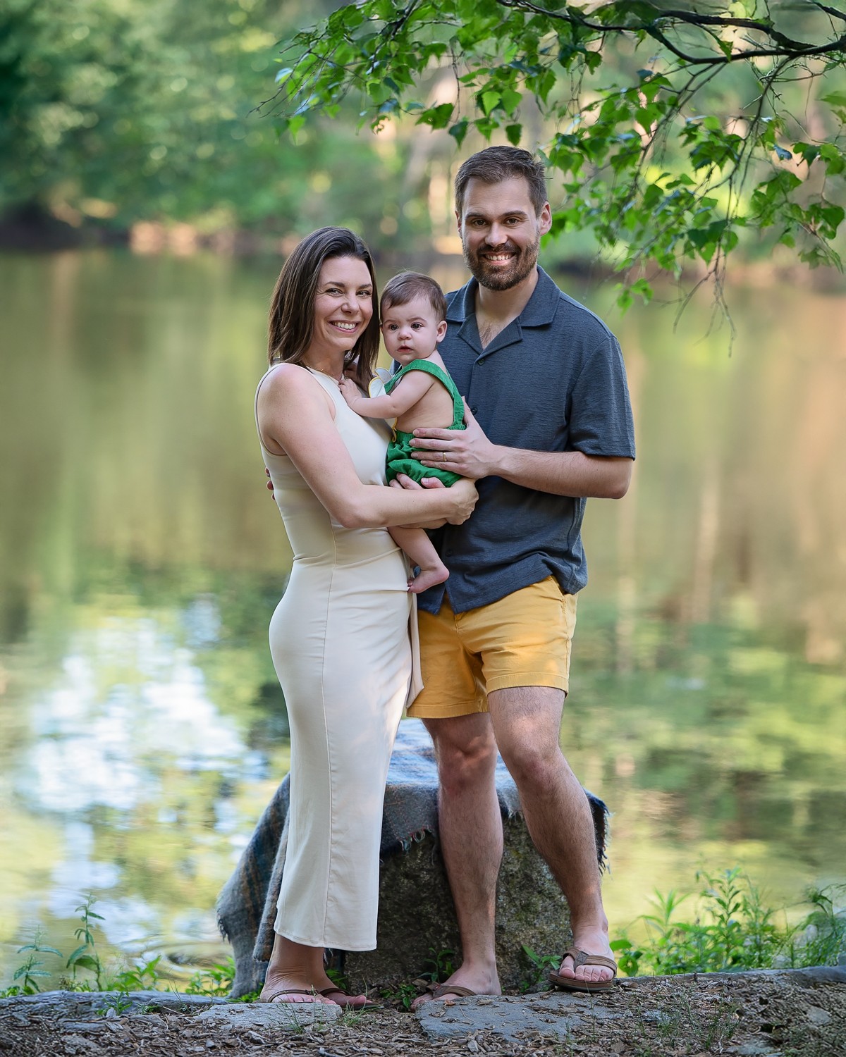 Family of three with a toddler beside Meadow Pond in summer at Great Brook Farm in Carlisle Massachusetts