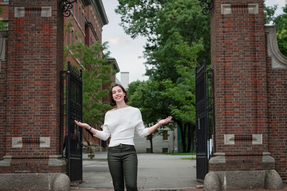 High school senior standing between the brick pillars of a wrought iron gate into Harvard Yard in Cambridge Massachusetts