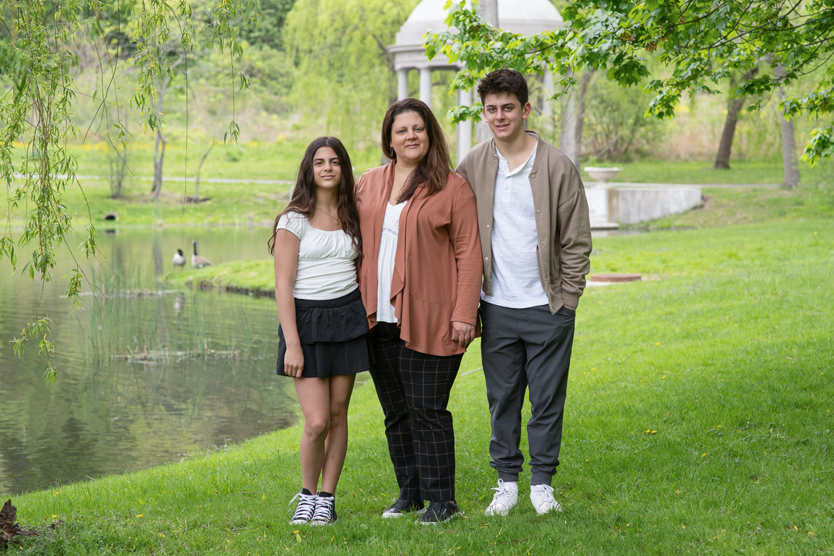 Mother standing with her teenage daughter and son on the lawn above the lagoon at Larz Anderson Park in Brookline Massachusetts