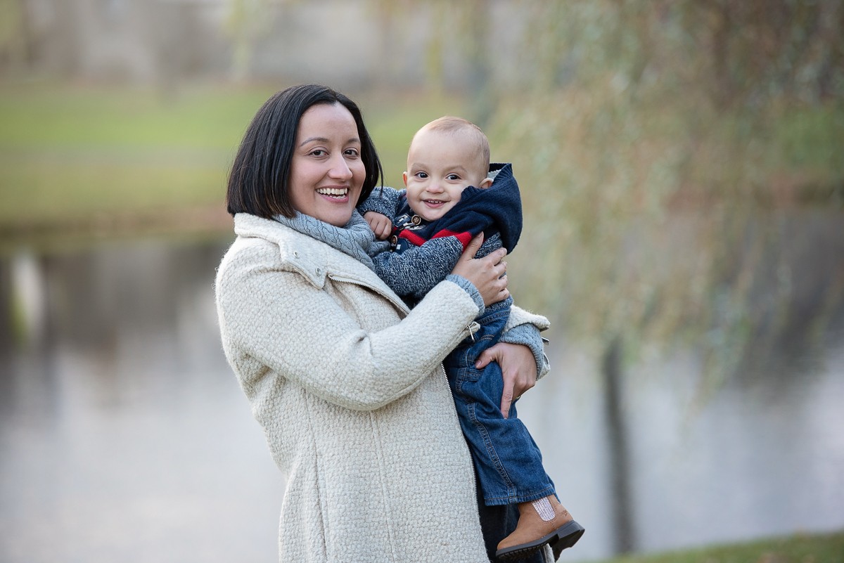 Mother holding her baby son on her hip at the edge of the lagoon at Larz Anderson Park in Brookline Massachusetts in autumn