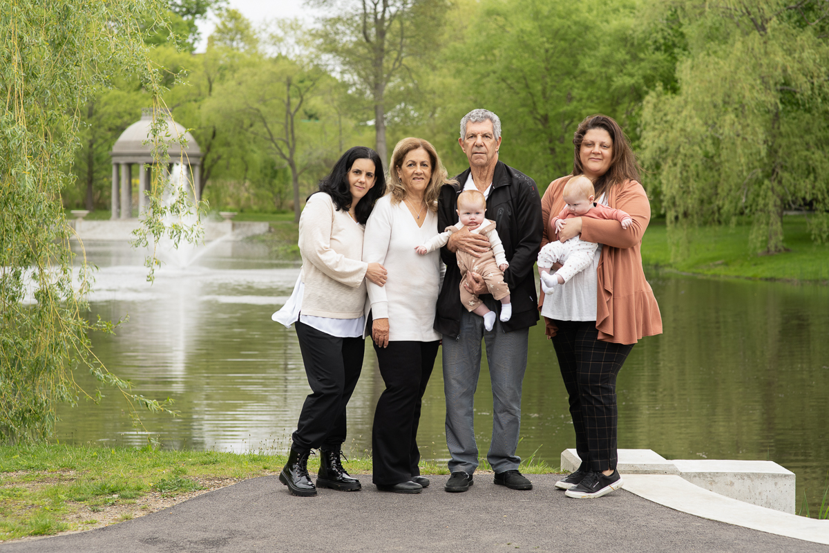 Three generations of one family holding two babies on the path beside the lagoon and fountain at Larz Anderson Park in Brookline MA