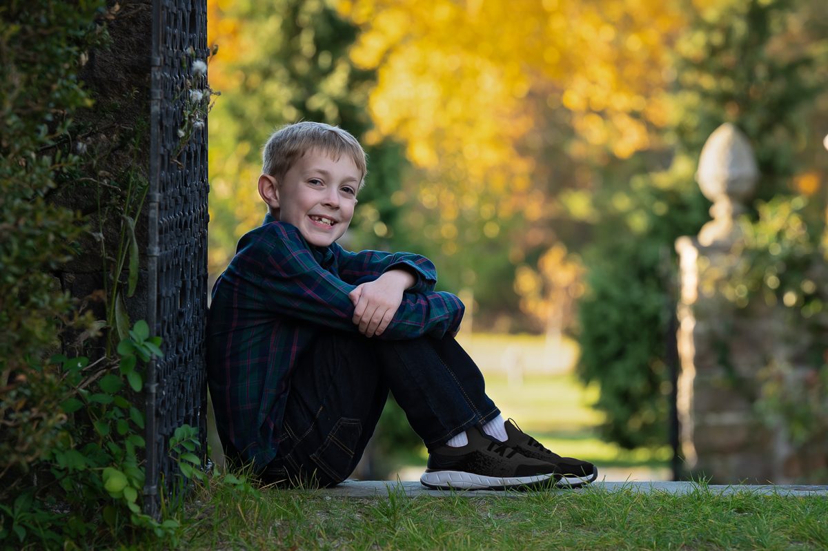 Young boy seated at the base of a stone gate pier with the garden path receding behind him at Stevens-Coolidge House and Gardens in North Andover MA