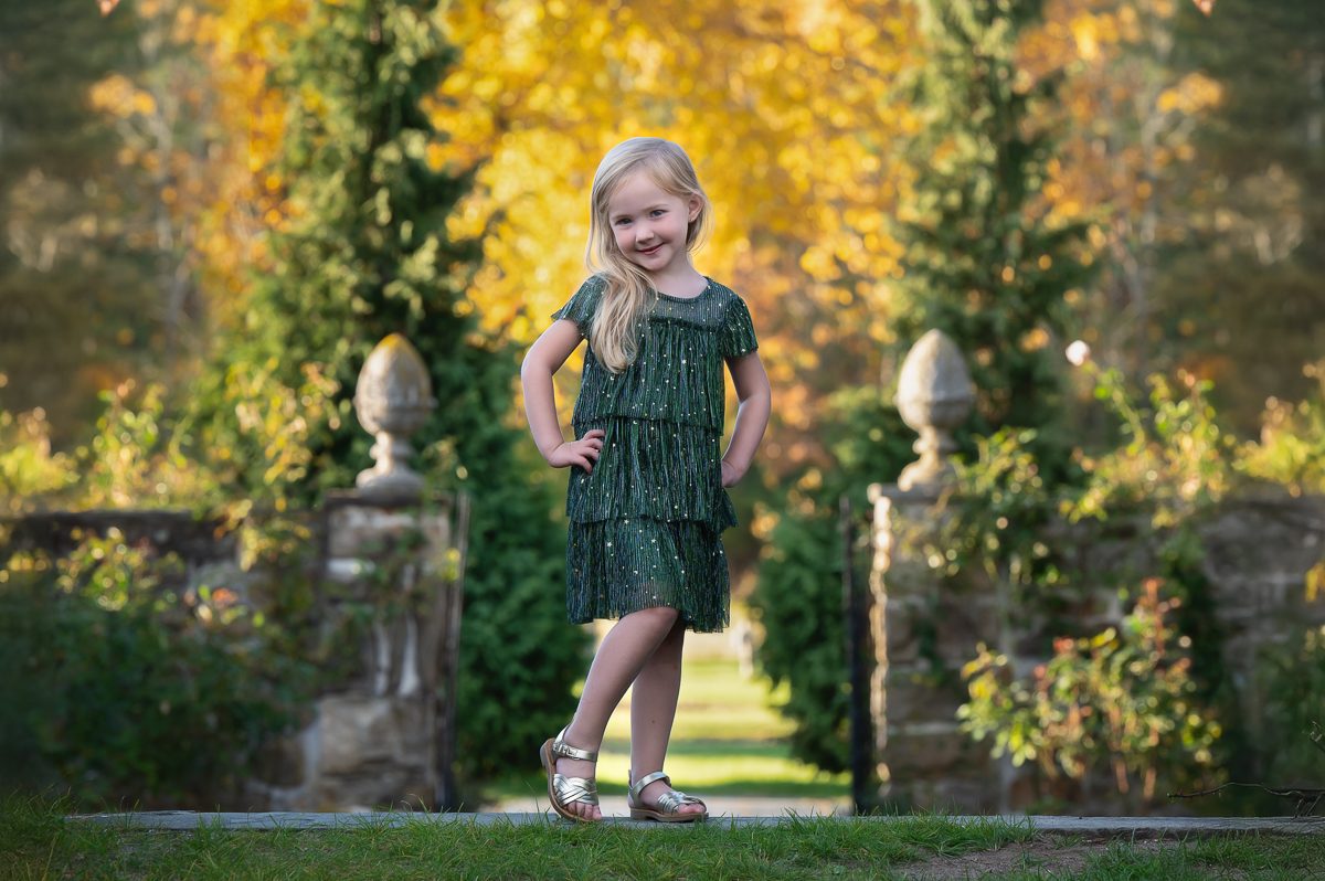 Young girl in a green dress standing on the path between the stone gate piers at Stevens-Coolidge House and Gardens in North Andover MA