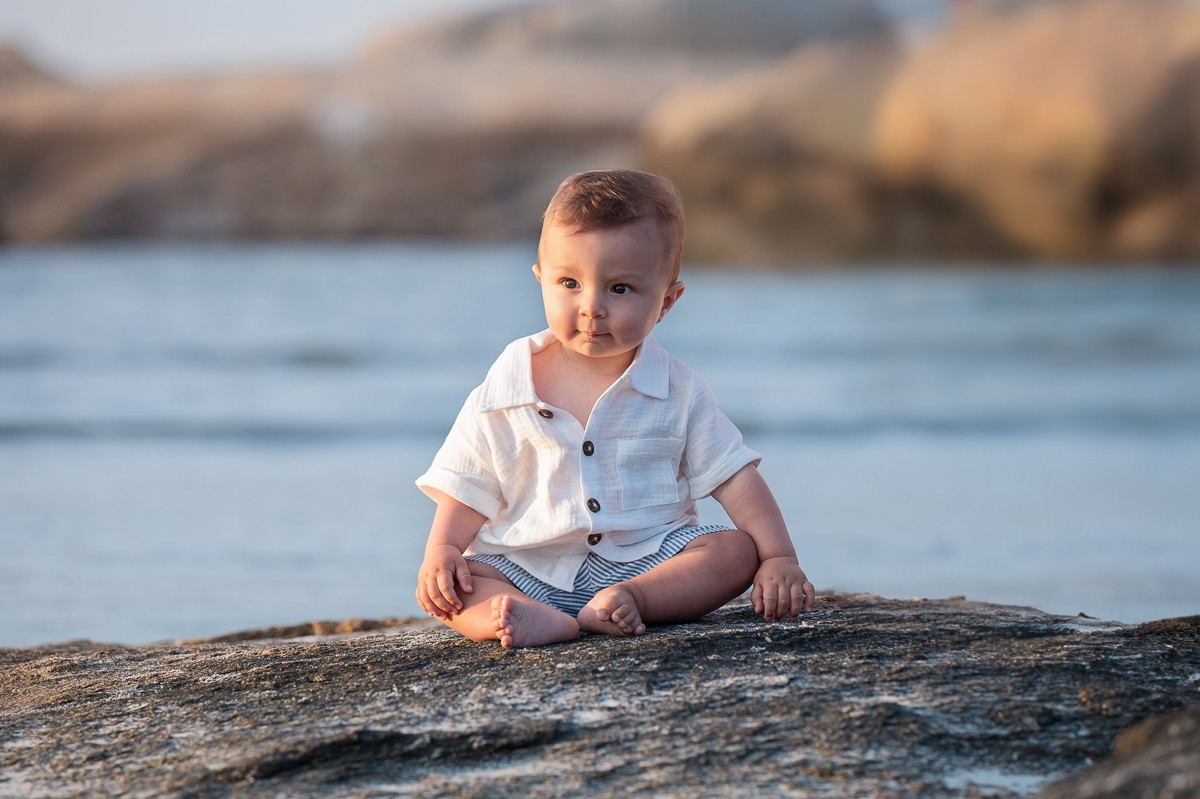 Baby sitting alone on a granite rock with the water behind at Wingaersheek Beach, Gloucester Massachusetts