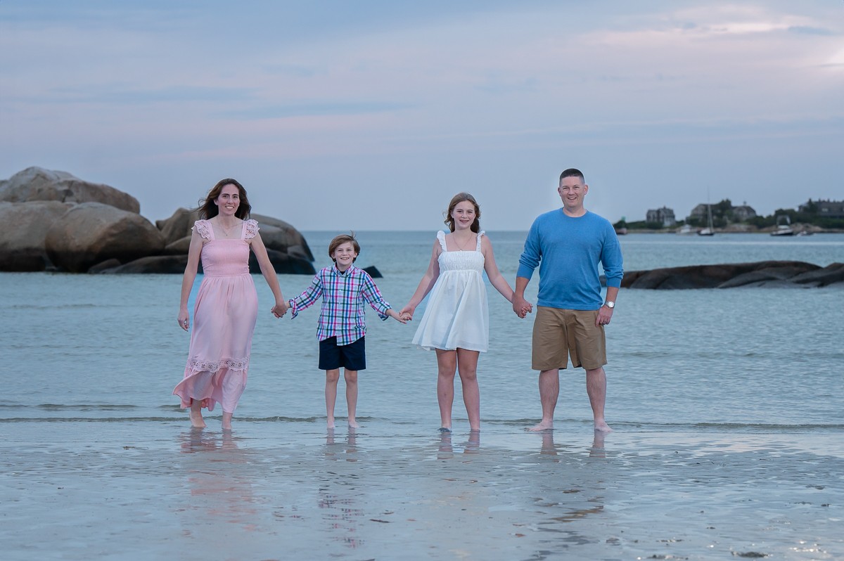 Family of four holding hands in the shallow water at low tide at Wingaersheek Beach in Gloucester MA