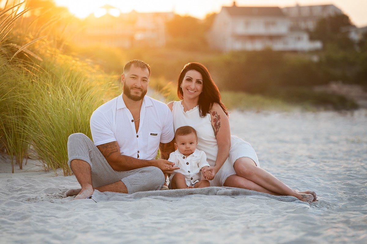 Parents seated in the dune grass with their baby at sunset at Wingaersheek Beach, Gloucester Massachusetts