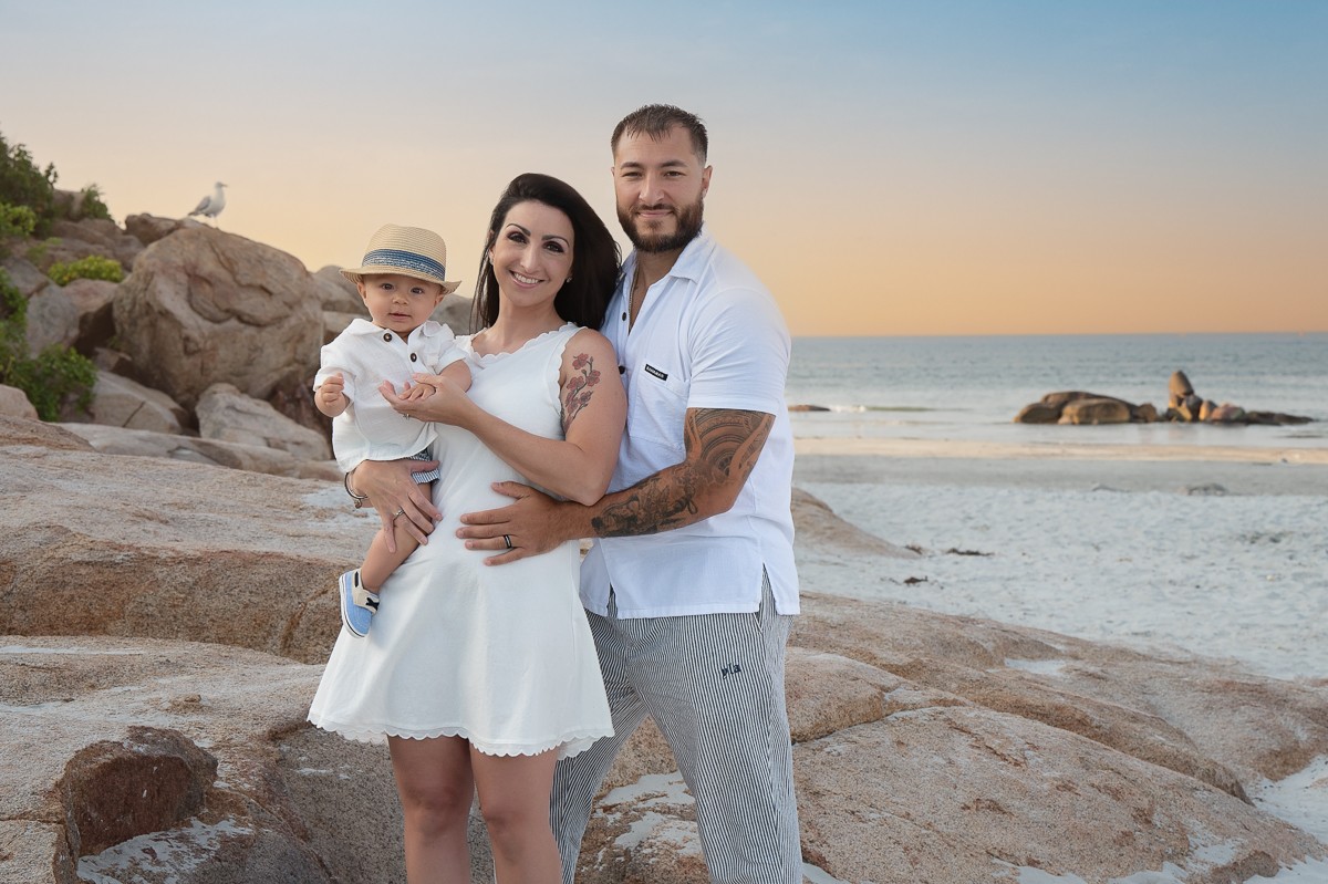 Family of three on the granite ledge at sunset with the sandbar behind them at Wingaersheek Beach, Gloucester MA