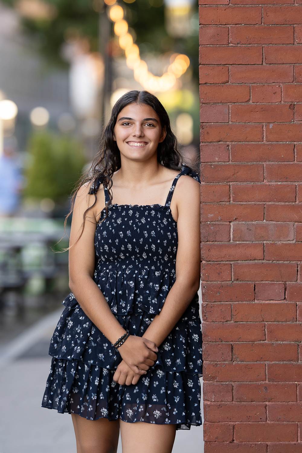 Smiling high school senior girl standing beside a red brick pillar on a downtown street in Lowell Massachusetts