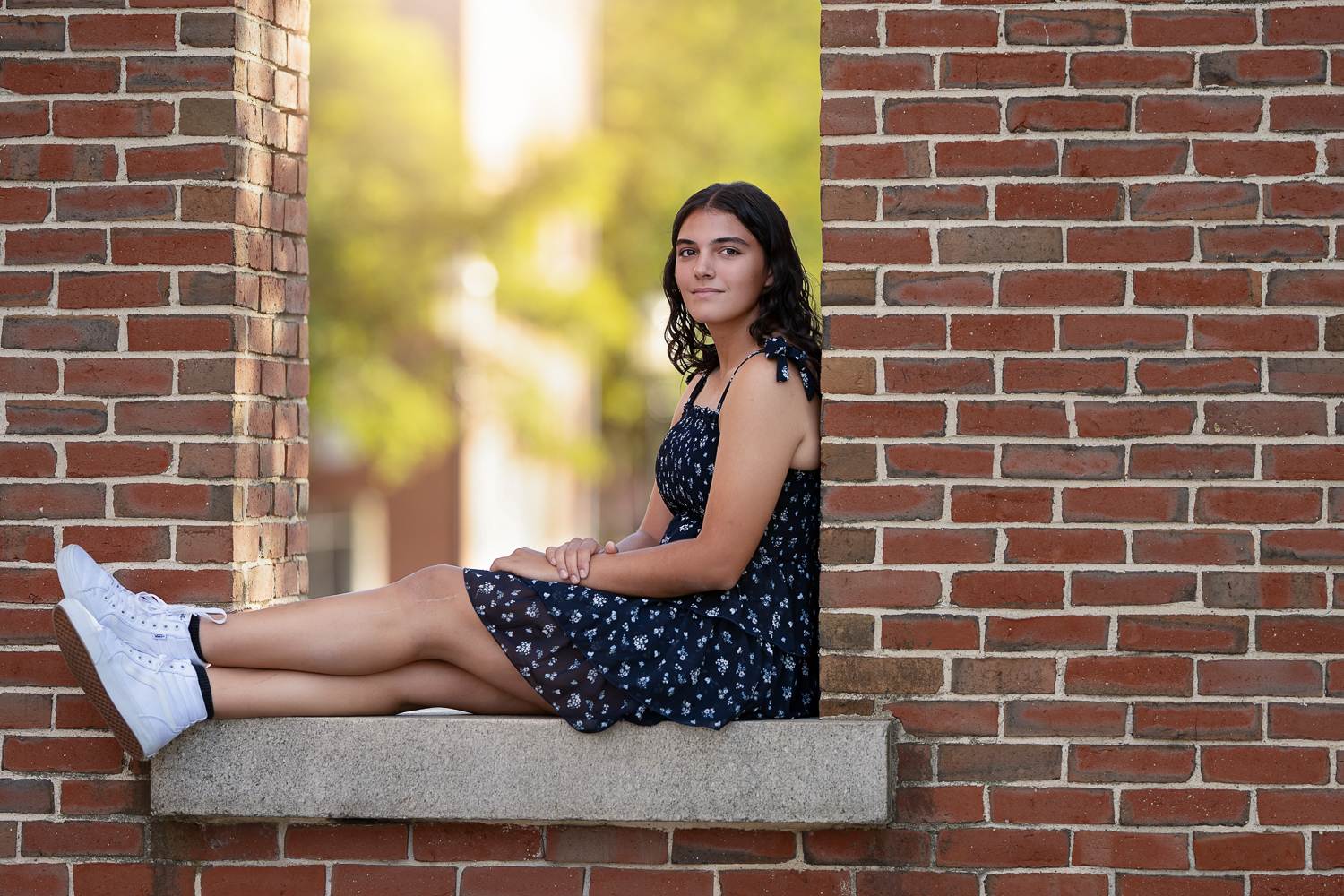 High school senior girl sitting on a granite ledge inside an open red brick window in downtown Lowell MA