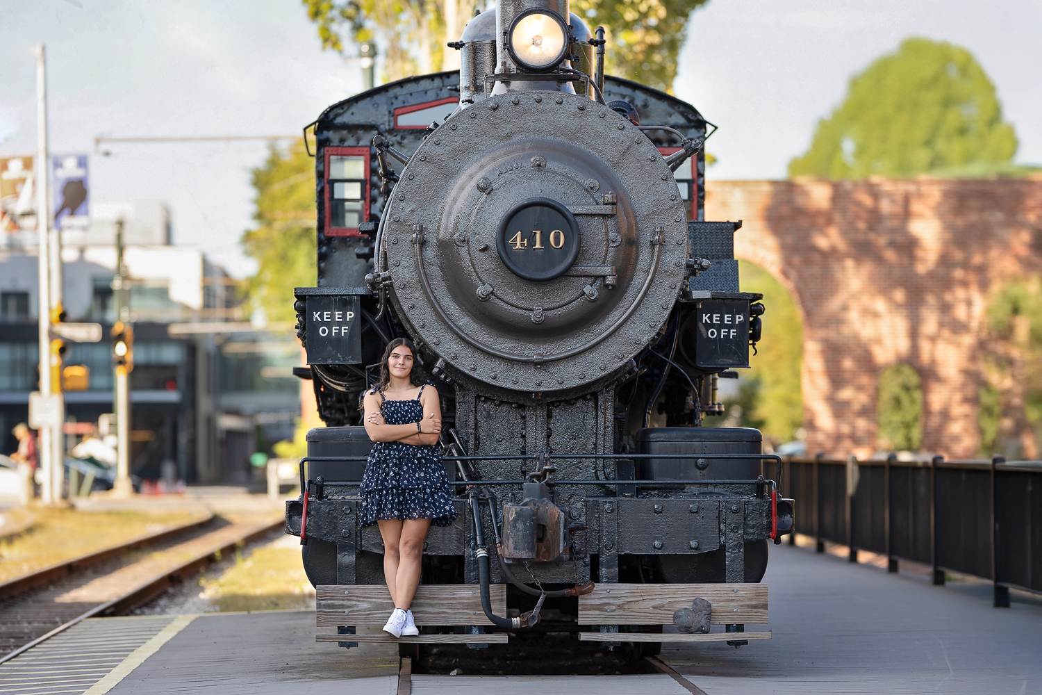 High school senior girl in a navy floral dress standing on the front of the black Boston and Maine 410 steam locomotive in Lowell MA